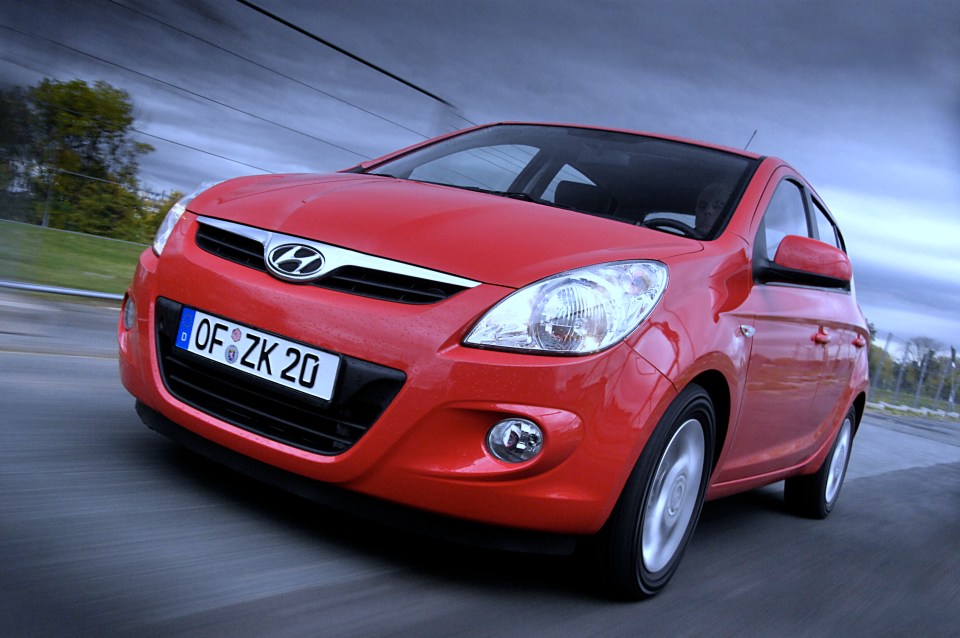 Red Hyundai i20 driving on a road.