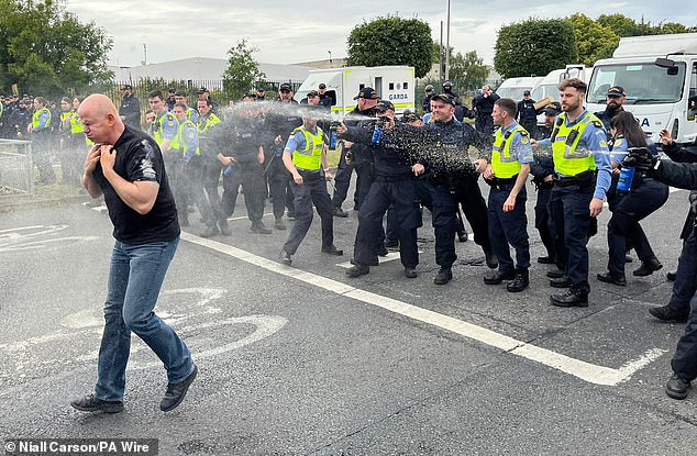 Gardai officers deploy pepper spray at a protester today after fires were started at the former site of the Crown Paints factory in Coolock, north Dublin in 2024