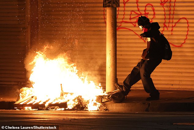 Pictured: A protester kicks a scooter into a fire amid ongoing protests