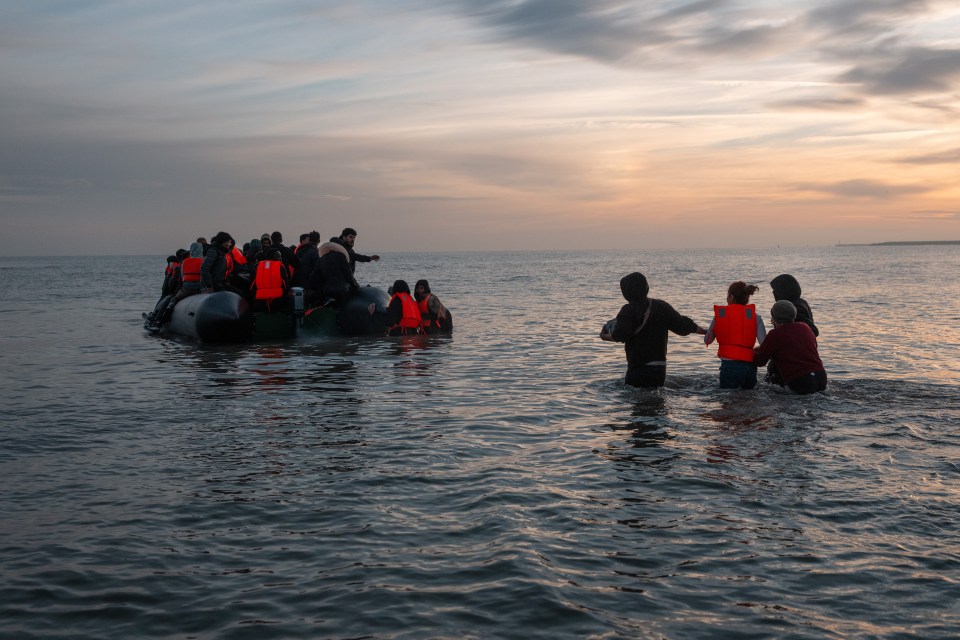 Migrants in a small boat approaching the shore at sunset.