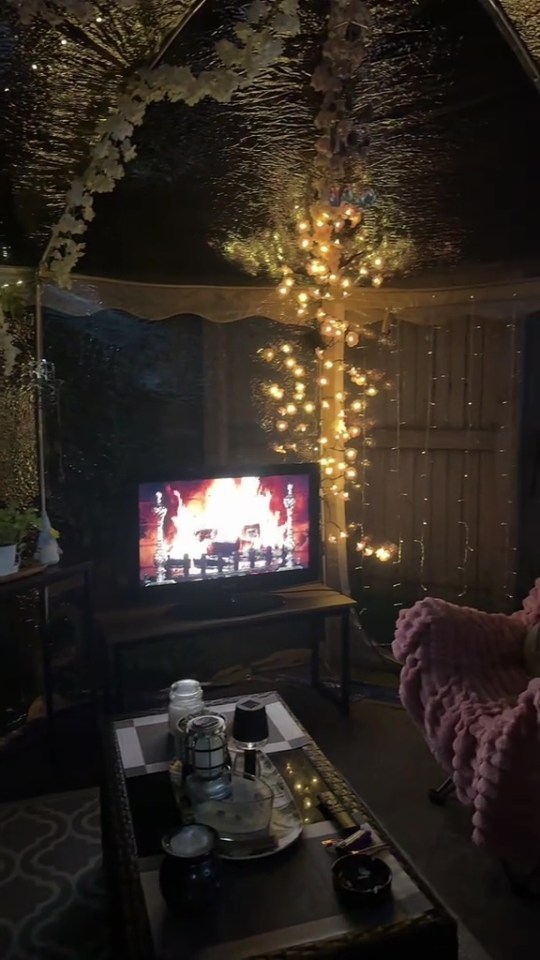 Cozy pop-up tent interior with a fireplace displayed on a TV screen and fairy lights.