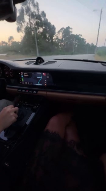 Interior view of a car driving, with a person's legs visible in the passenger seat.