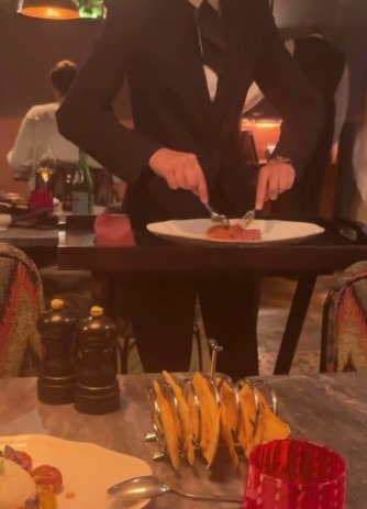 Waiter serving raw meat dish at a restaurant table.