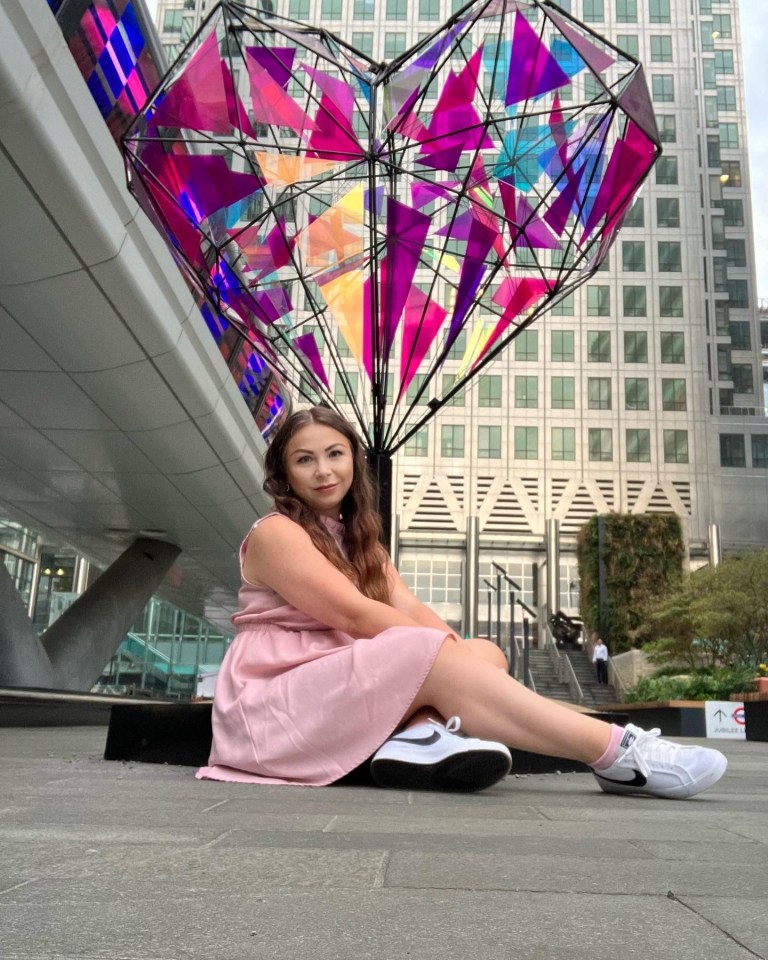 Woman in pink dress sitting in front of a large heart-shaped sculpture.
