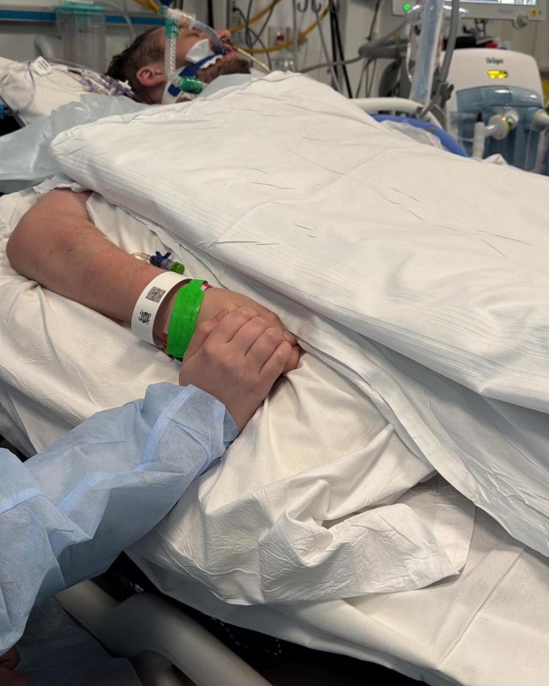 A woman holding the hand of a man lying in a hospital bed.