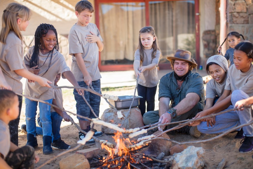 Children and an adult roasting bread over a campfire.