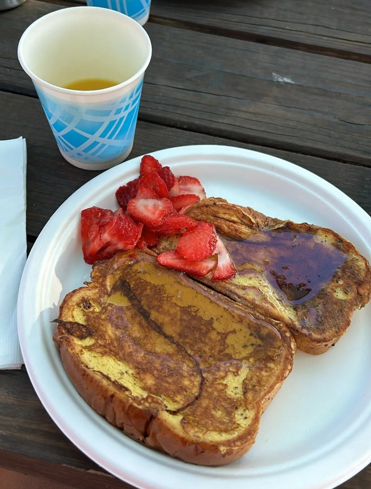 French toast with strawberries and syrup on a plate with drinks.