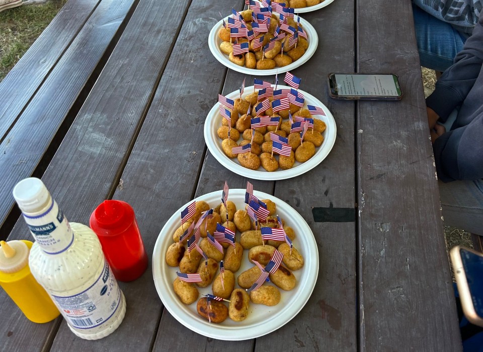 Corn dogs with small American flags on a picnic table.