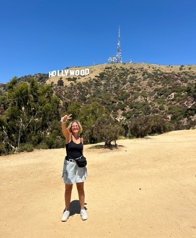 Person giving peace sign in front of the Hollywood sign.