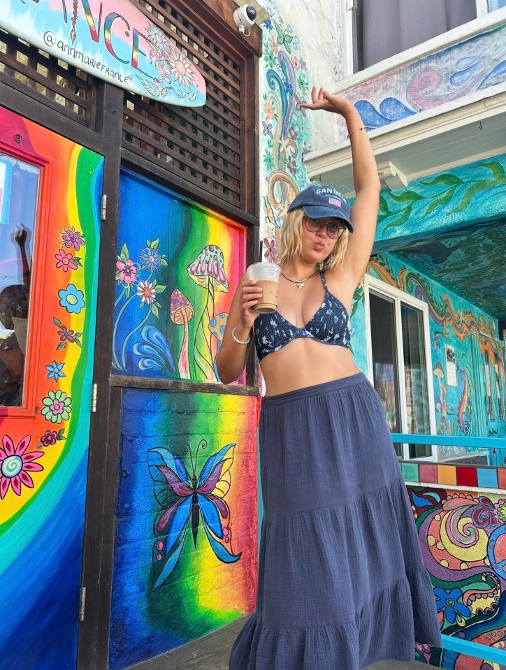 Woman in San Diego holding a coffee cup in front of colorful painted building.