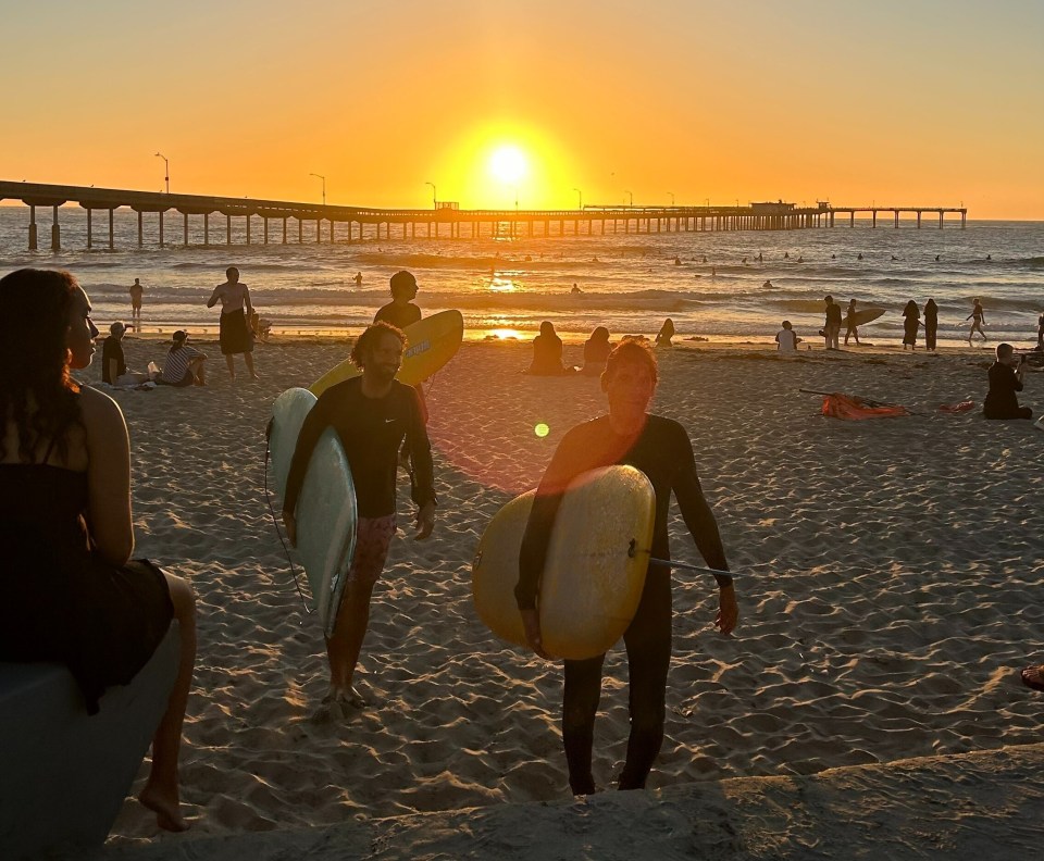 Sunset at the beach with surfers carrying boards.