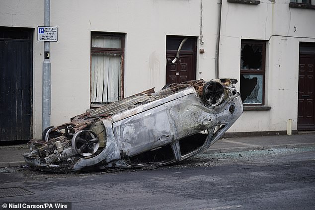 A burnt-out overturned car on the street today after a second night of violence in Ballymena