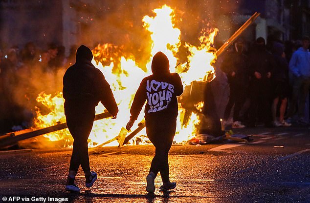 Protestors walk past a fire set in a street of Ballymena, Northern Ireland as riots raged through the town