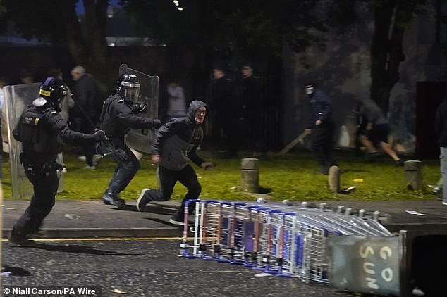 Riot police wearing armour and carrying shields chase down a protestor in Ballymena