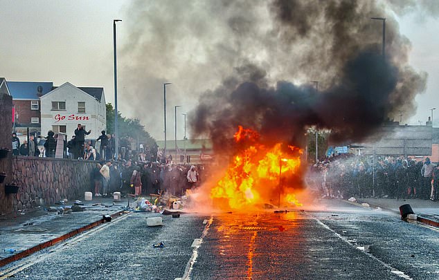 A huge fire erupts in the middle of the street surrounded by protesters in Northern Ireland on Tuesday