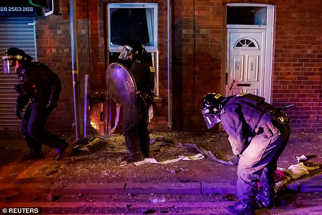 Police officers stands in front of a house after demonstrators vandalised it during the second night of mayhem