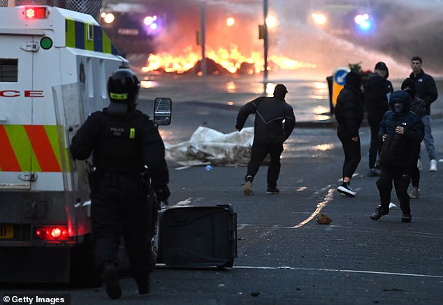 Masked yobs face riot police on the street in the town centre, which has been set on fire