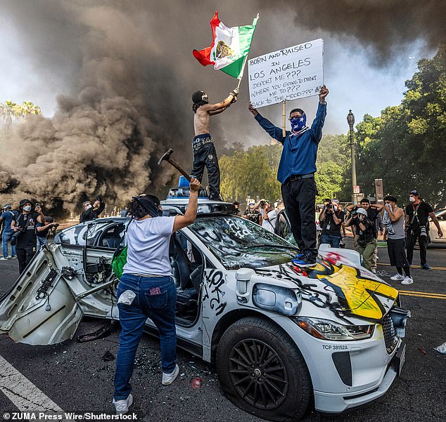Protesters in Los Angeles are seen climbing atop a destroyed car