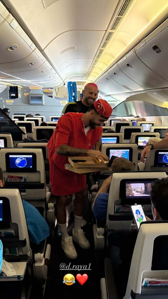Man in red distributing pizza on airplane.