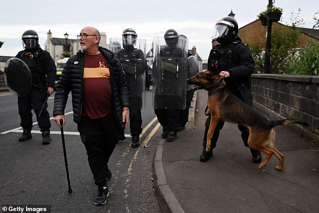 A resident walks past PSNI riot squad officers and a dog handler as police form a blockade in Ballymena
