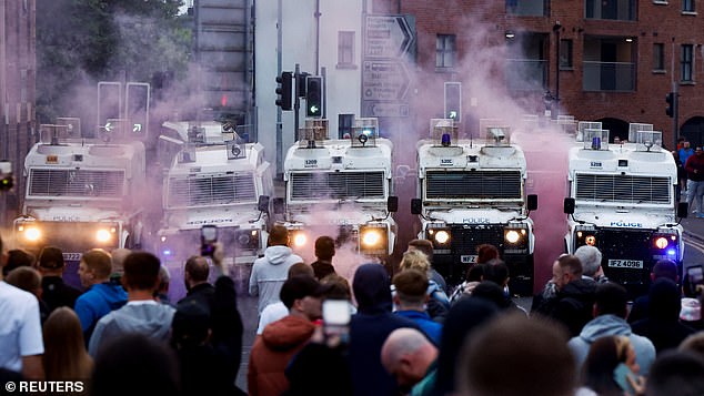 Coloured smoke billows as demonstrators gather in front of riot police vehicles in Ballymena