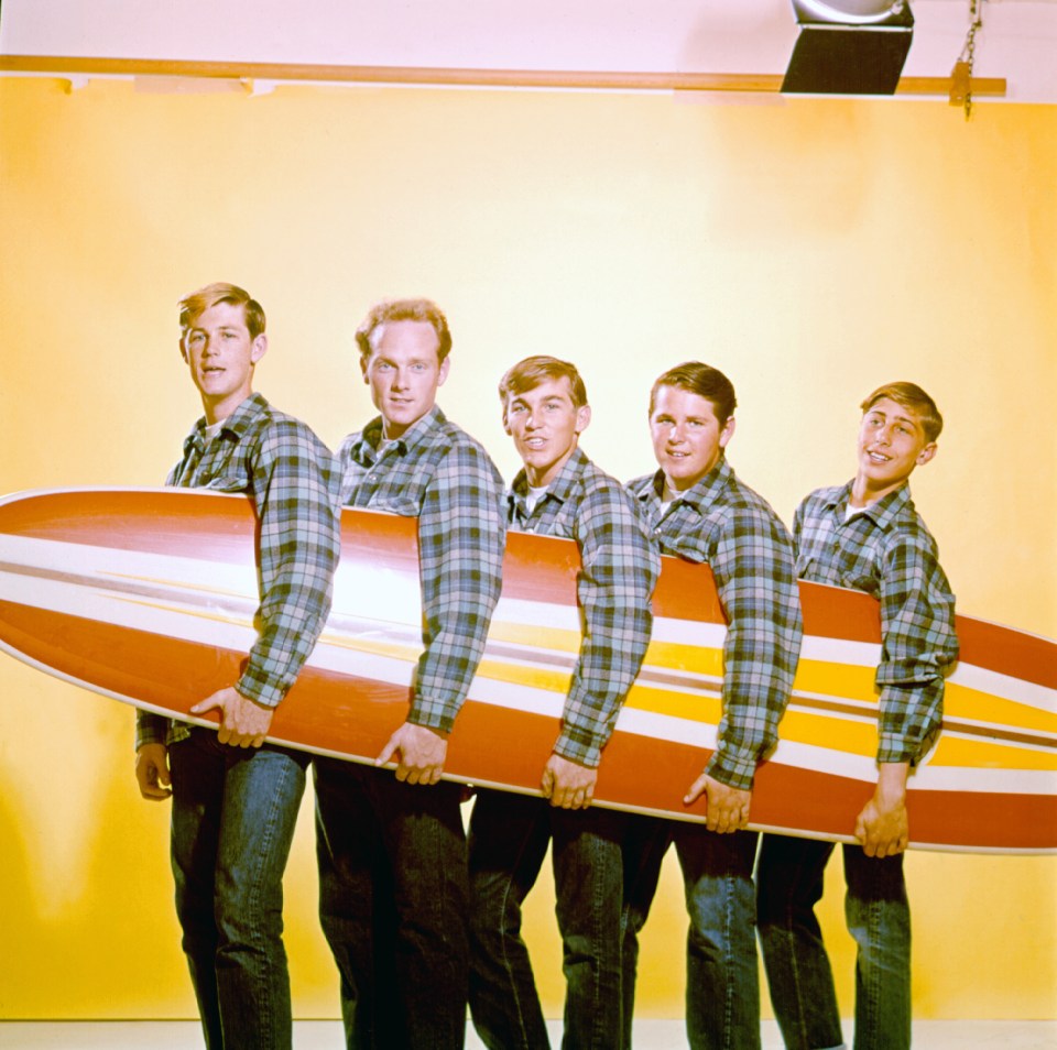 The Beach Boys posing with a surfboard.