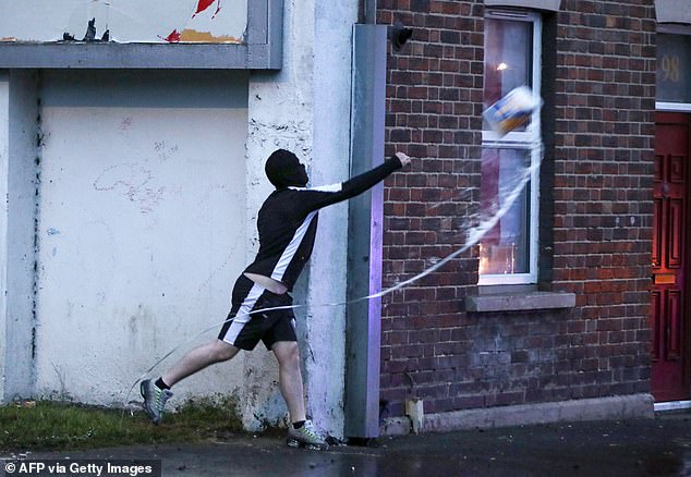 A masked protestor throws an item at Riot Police during a third night of demonstrations in Northern Ireland