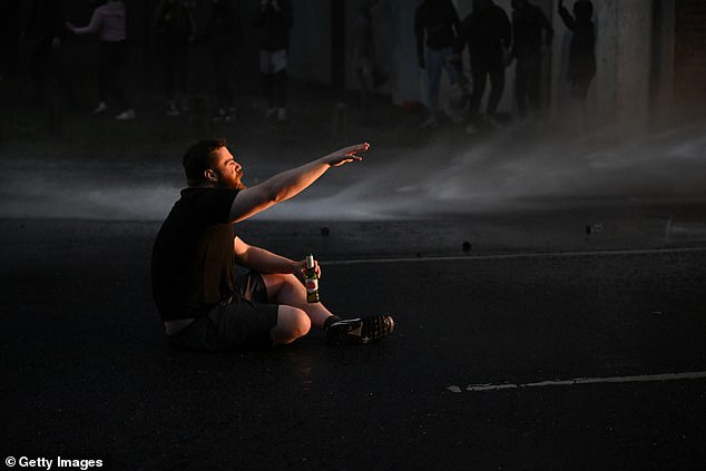 A man sits with a drink opposite riot police vehicles on the third night of unrest in Ballymena