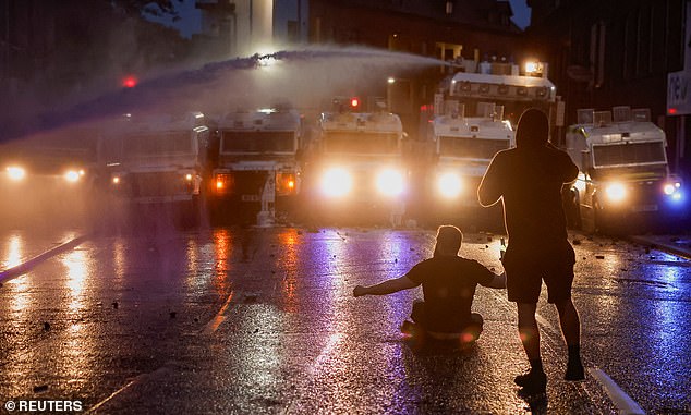 A demonstrator sits down opposite a row of riot police vehicles in Ballymena