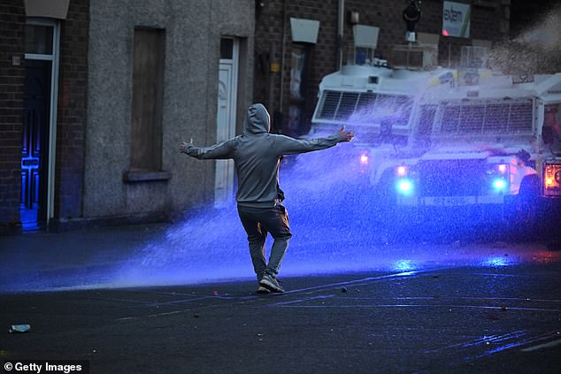 A member of the crowd gestures towards the PSNI riot squad officers