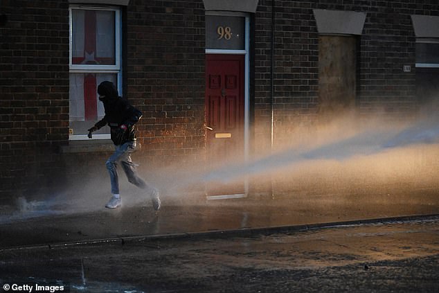 A member of the crowd runs away while being sprayed with water from a cannon by the PSNI riot squad