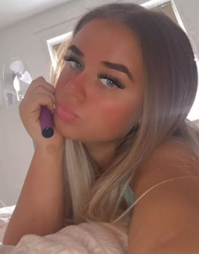 Close-up selfie of a young woman holding a purple vape pen.
