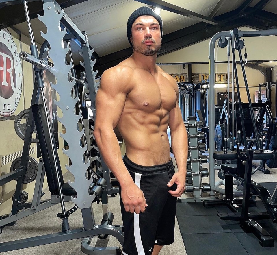 Muscular man in gym, wearing a beanie and shorts.