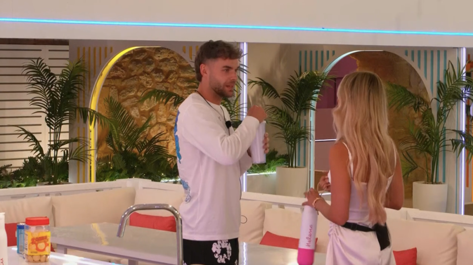 Screenshot of a man and woman talking in a brightly lit room.