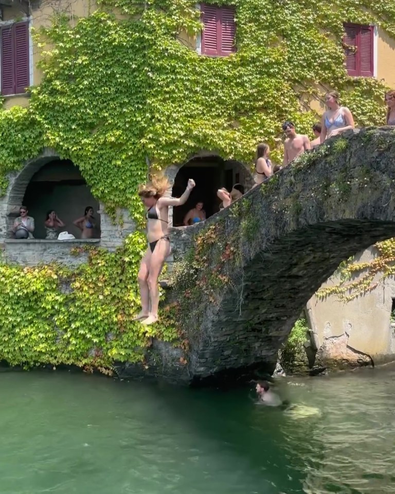 Woman jumping off a stone bridge into water.