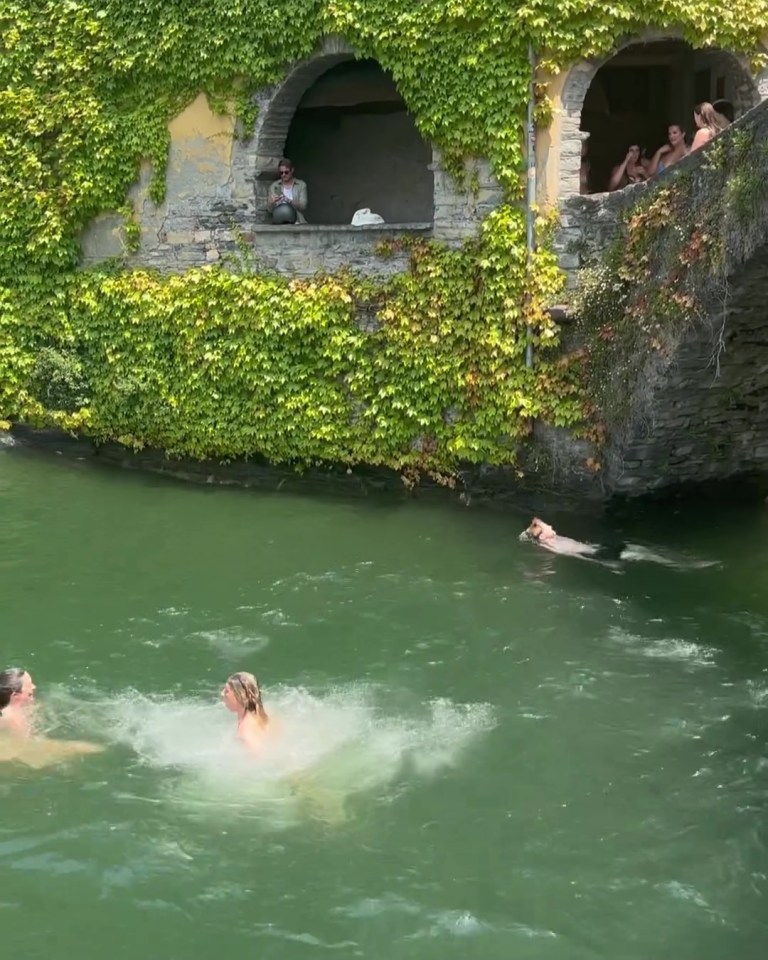 People jumping into a lake from a stone structure covered in ivy.