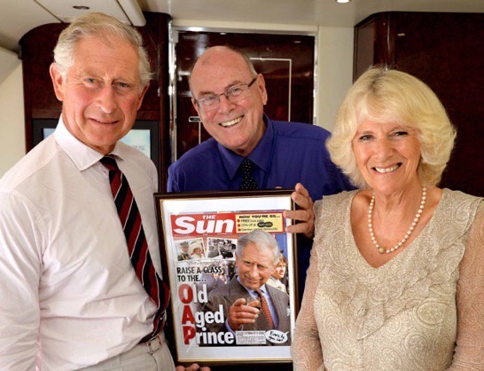 King Charles III, Camilla, Queen Consort, and Arthur Edwards holding a framed newspaper clipping.