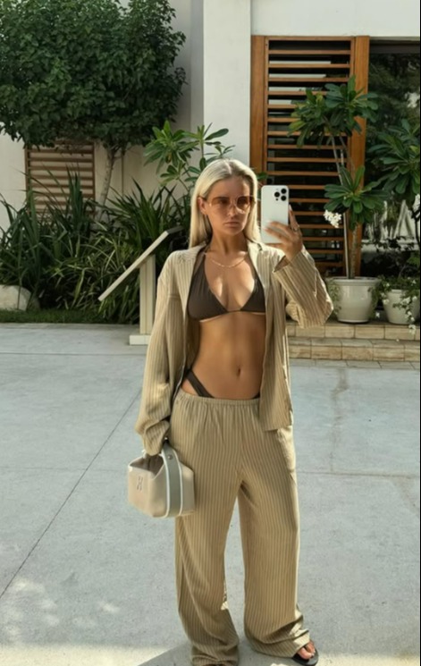 Woman in beige pinstripe pants and matching shirt taking a selfie.