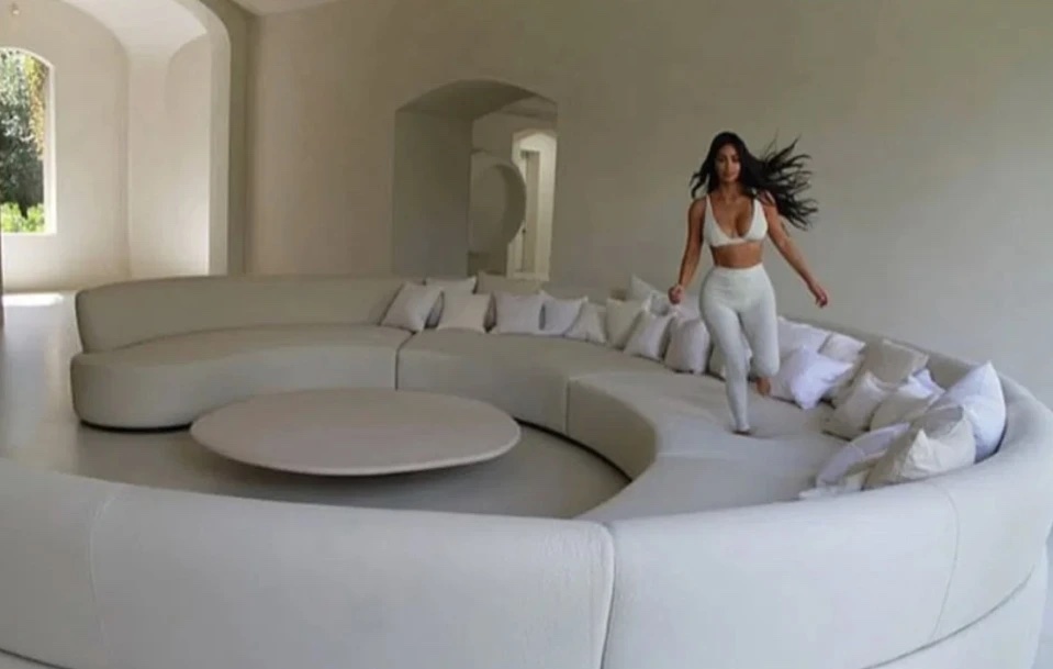 Kim Kardashian running across a large circular beige couch in her home.