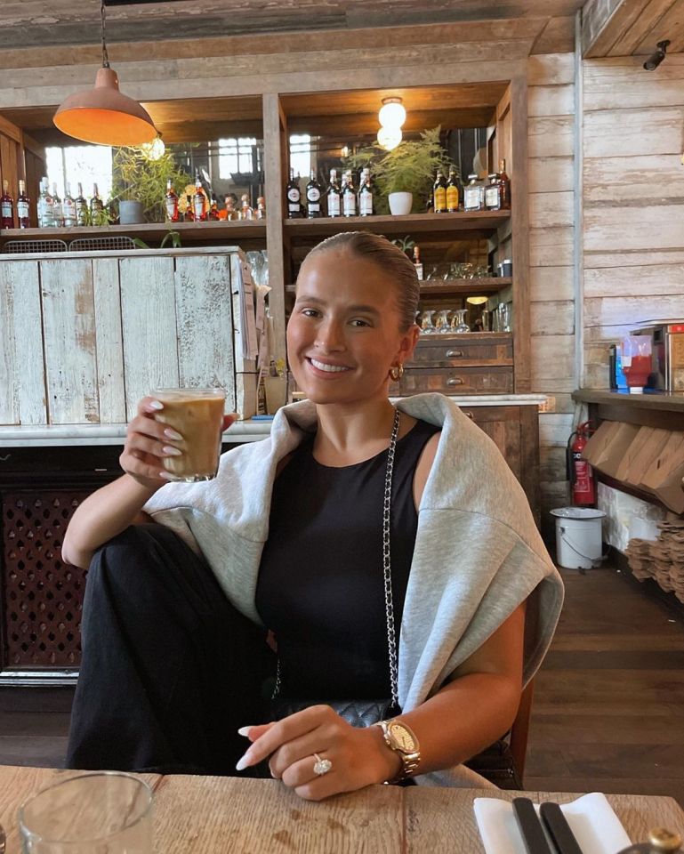 Woman showing off engagement ring while holding a coffee.
