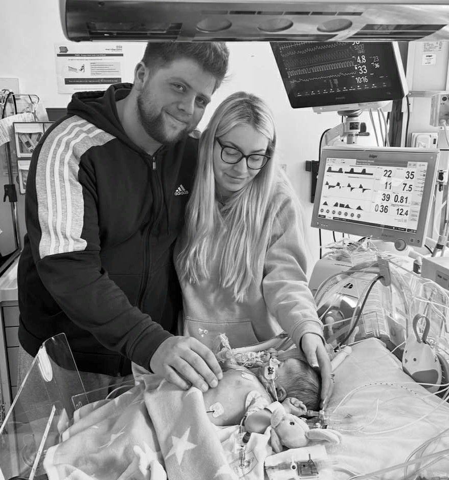 Black and white photo of parents holding their baby in a hospital incubator.