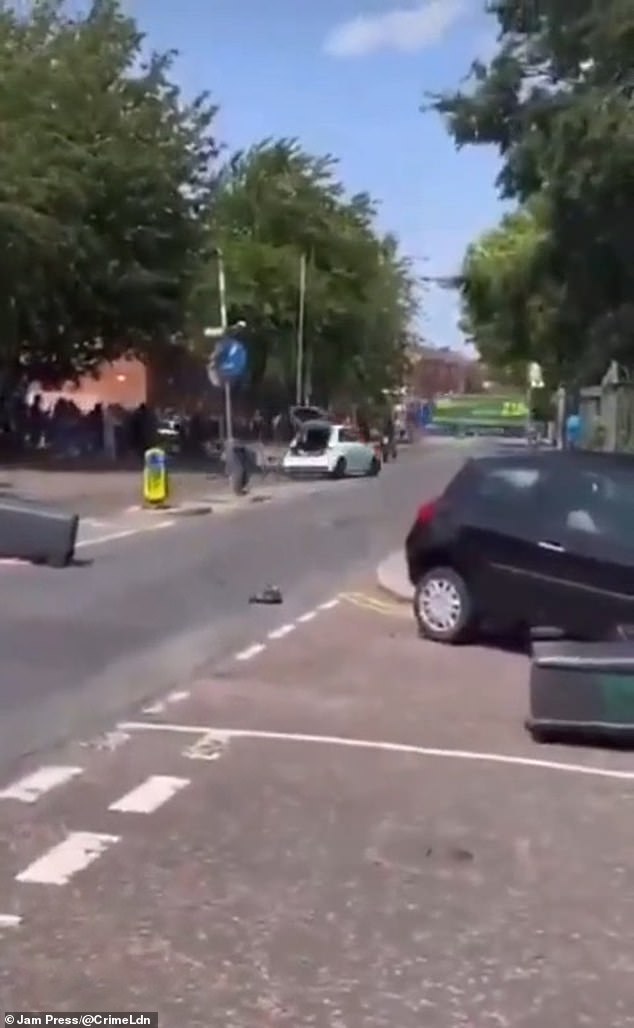 The large group of 60 masked youths watched on as the car - which was missing its bumper - mounted the kerb and swerved on a grass verge, narrowly missing the crowd
