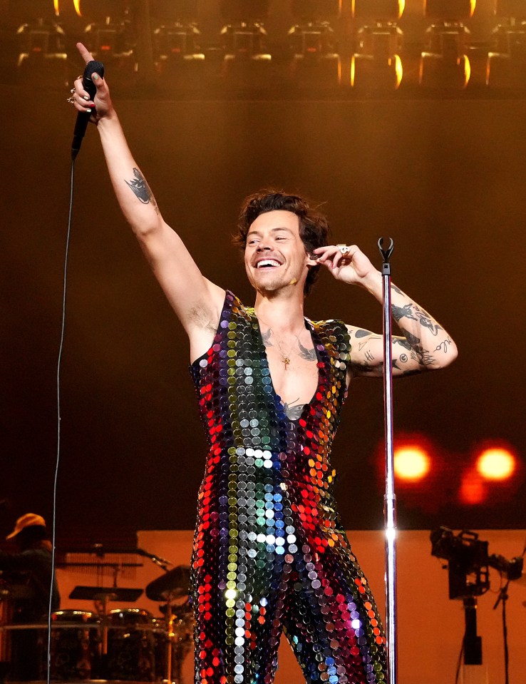 Harry Styles performing onstage at Coachella in a rainbow sequin jumpsuit.