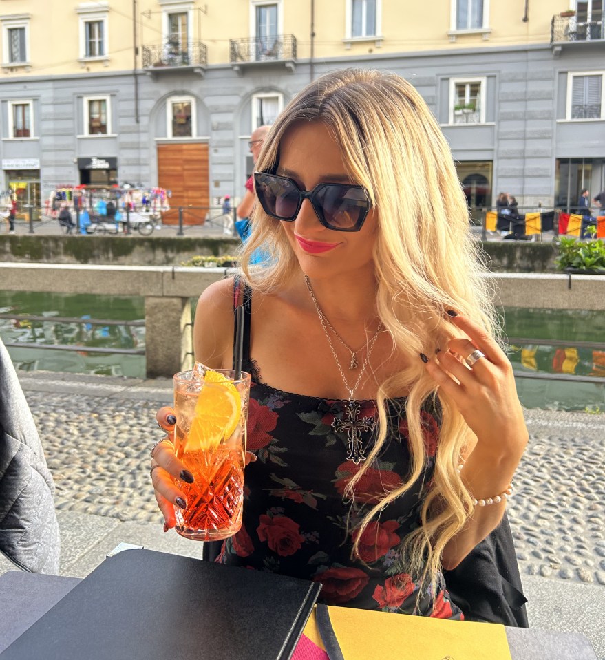 Woman with long blonde hair holding an Aperol Spritz at an outdoor cafe.
