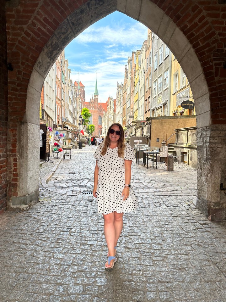 Woman in polka dot dress walking down a cobblestone street in a European city.