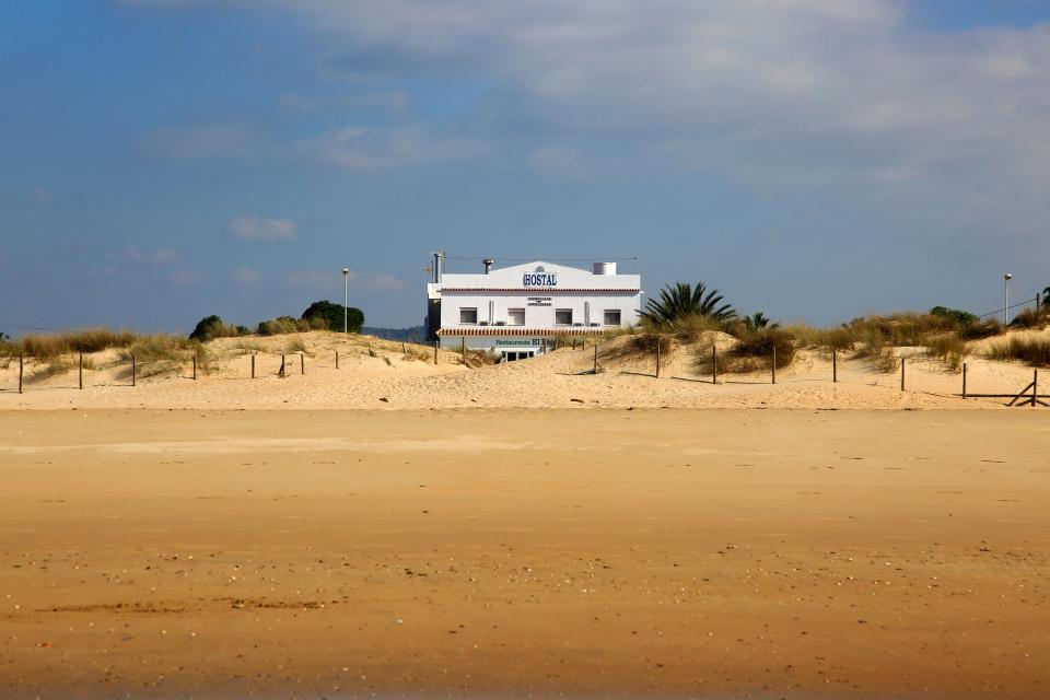 A white beach hotel behind sand dunes.