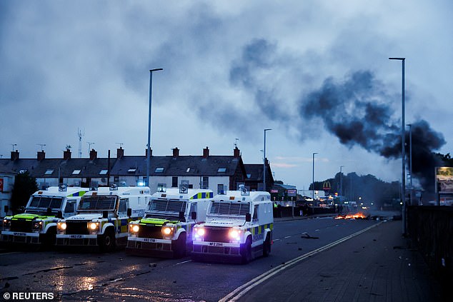 Police vehicles are parked as flames rise during a second night of riots, in Ballymena, Northern Ireland, June 10