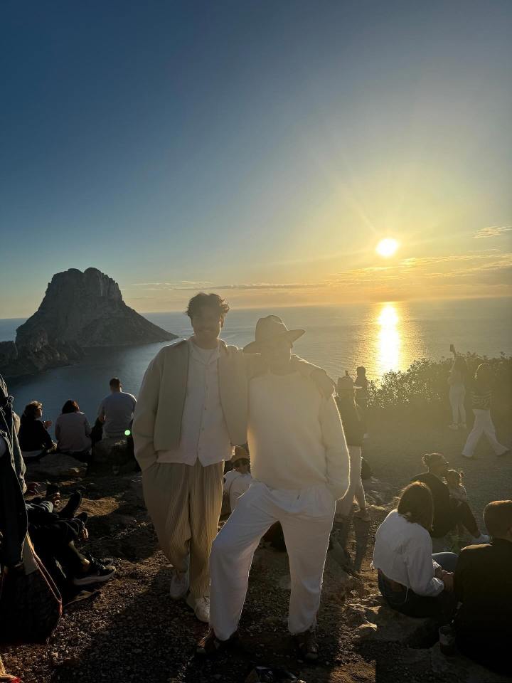 Two men standing together at sunset overlooking the ocean.