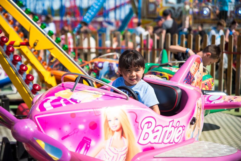 Girl riding a pink Barbie airplane ride at an amusement park.