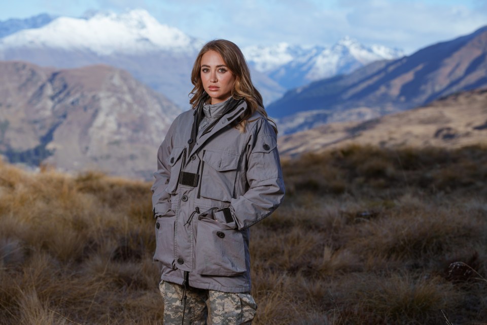 Georgia Harrison in a gray jacket, standing in a field with mountains in the background.